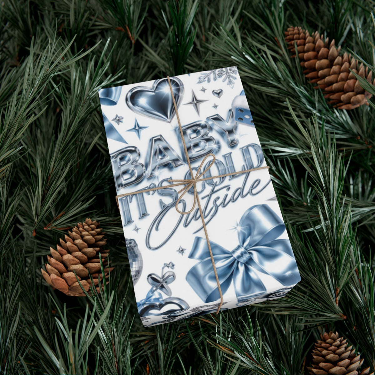 Gift wrapped in Baby It's Cold Y2K Christmas paper with chrome lettering, icy blue bows and hearts, tied with twine on pine branches