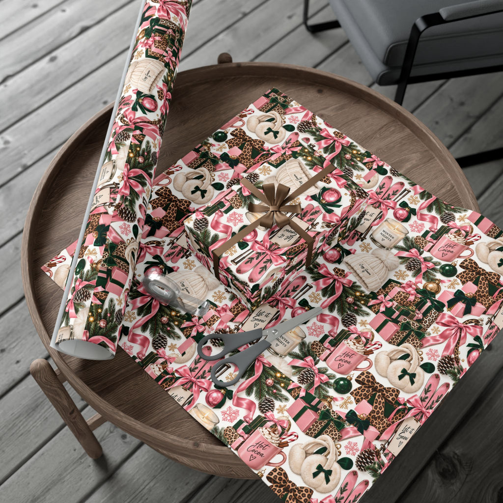 Cozy Season Christmas wrapping paper roll and gifts on a wooden tray, with pink bows, leopard accents and emerald-green holiday motifs